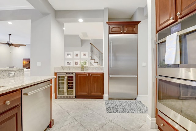 kitchen with light tile patterned floors, beverage cooler, a ceiling fan, appliances with stainless steel finishes, and light stone counters