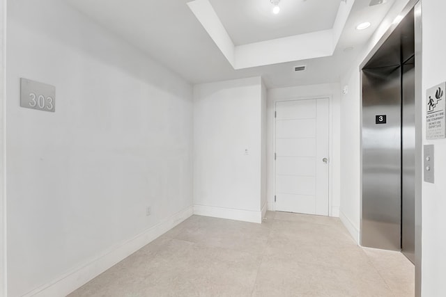 interior space with baseboards, a tray ceiling, visible vents, and elevator