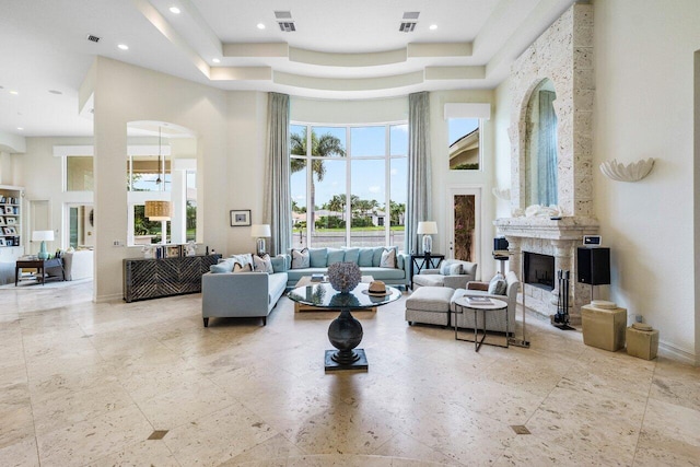 living room featuring a tray ceiling, visible vents, a fireplace, and a towering ceiling