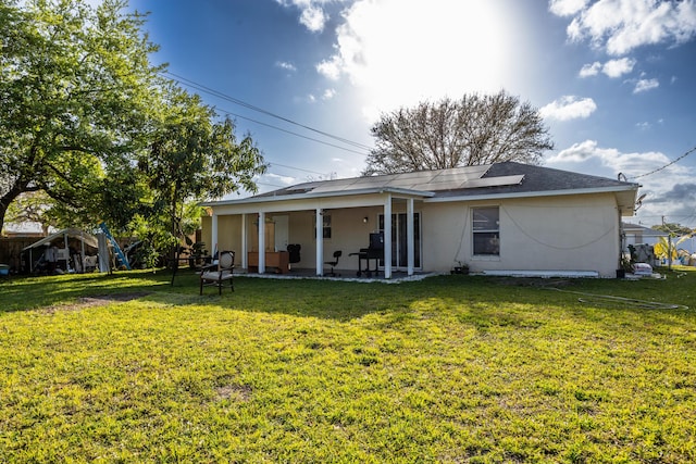 back of property with solar panels, a lawn, a patio, and stucco siding