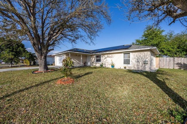 ranch-style home with solar panels, an attached garage, fence, and a front yard