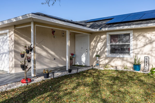 view of exterior entry with roof with shingles, roof mounted solar panels, a lawn, and stucco siding