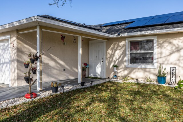 ranch-style house with solar panels, a front lawn, an attached garage, and stucco siding