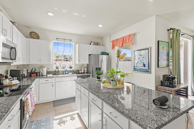 kitchen featuring appliances with stainless steel finishes, white cabinets, a kitchen island, a sink, and dark stone counters