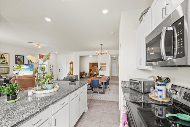 kitchen featuring light tile patterned floors, stainless steel appliances, an inviting chandelier, open floor plan, and white cabinets