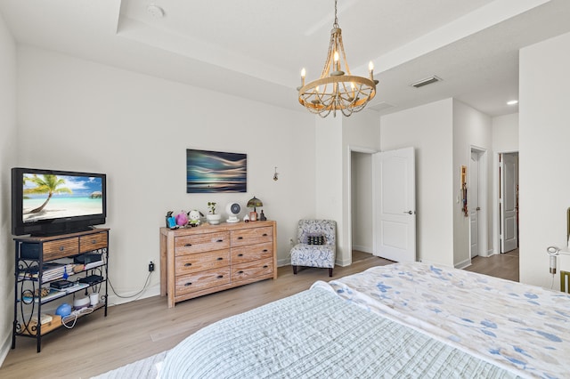 bedroom with a tray ceiling, visible vents, an inviting chandelier, and wood finished floors