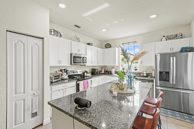 kitchen with dark stone counters, stainless steel appliances, a kitchen island, and white cabinetry