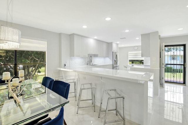 kitchen featuring a breakfast bar, stainless steel refrigerator with ice dispenser, white cabinets, a sink, and a peninsula