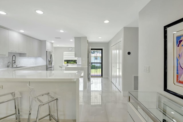 kitchen featuring stainless steel fridge with ice dispenser, light countertops, a kitchen bar, white cabinetry, and a sink