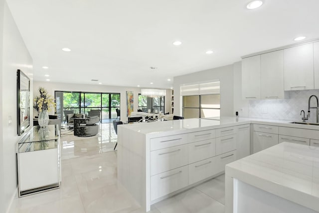 kitchen with decorative backsplash, white cabinets, modern cabinets, a peninsula, and a sink