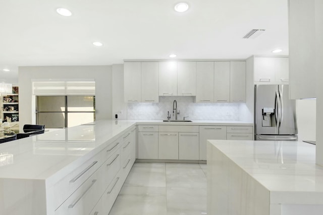 kitchen with stainless steel fridge, white cabinets, modern cabinets, a peninsula, and a sink