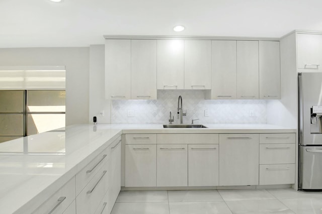 kitchen featuring light countertops, decorative backsplash, a sink, stainless steel fridge, and a peninsula