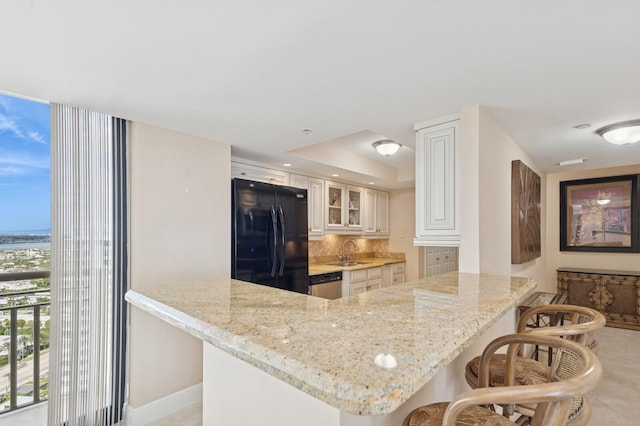 kitchen with a breakfast bar area, freestanding refrigerator, a sink, dishwasher, and a peninsula