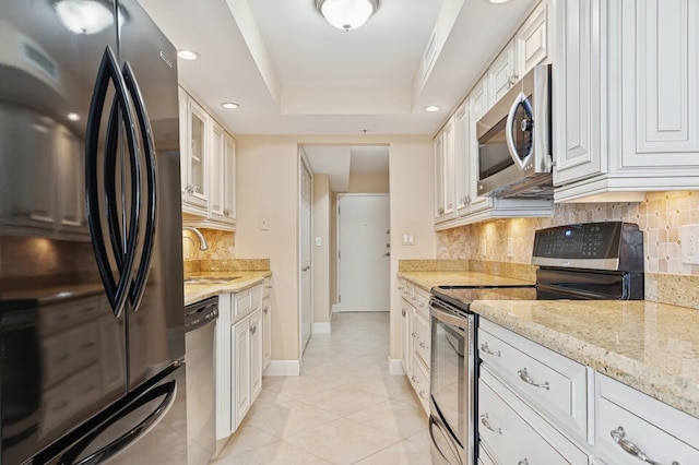 kitchen with tasteful backsplash, a tray ceiling, stainless steel appliances, and a sink