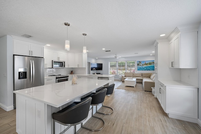 kitchen featuring stainless steel appliances, visible vents, white cabinetry, open floor plan, and backsplash