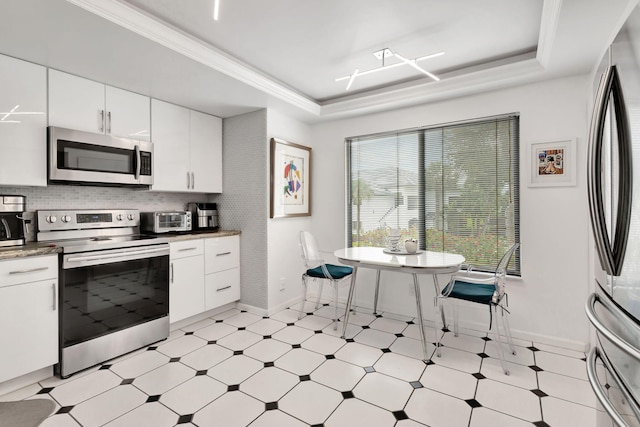 kitchen with baseboards, a raised ceiling, appliances with stainless steel finishes, light floors, and white cabinetry