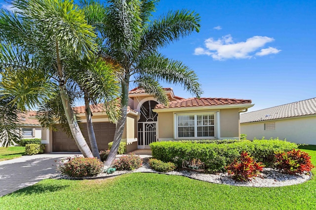 mediterranean / spanish house featuring driveway, a garage, a tiled roof, a front lawn, and stucco siding