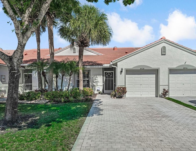 view of front of house featuring an attached garage, a tiled roof, decorative driveway, stucco siding, and a front lawn