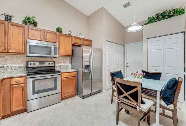 kitchen with appliances with stainless steel finishes, backsplash, light stone countertops, and brown cabinets