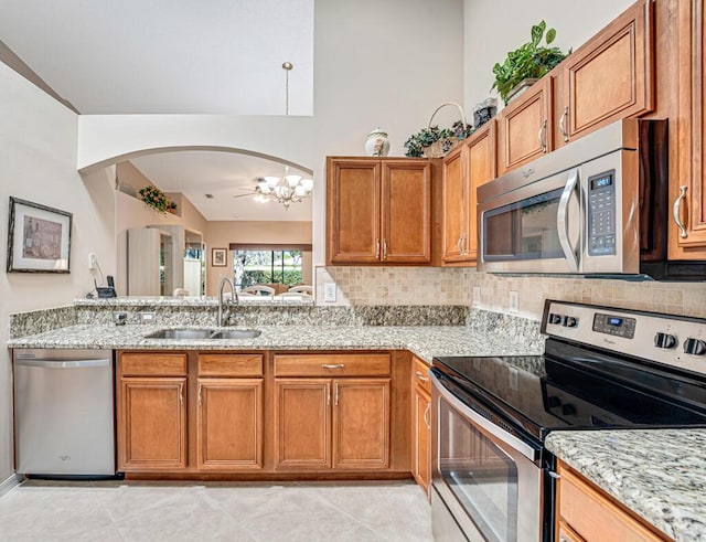 kitchen with light stone counters, brown cabinets, stainless steel appliances, backsplash, and a sink