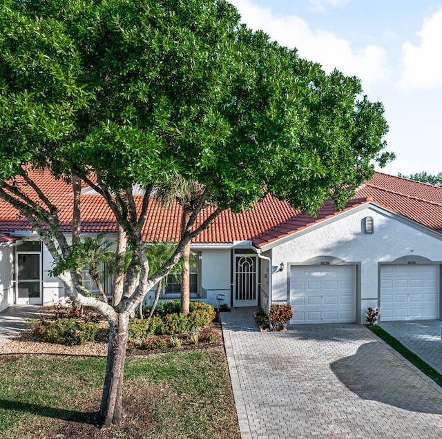 mediterranean / spanish home featuring an attached garage, a tiled roof, decorative driveway, and stucco siding