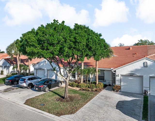 view of front facade with a garage, a tile roof, decorative driveway, and stucco siding