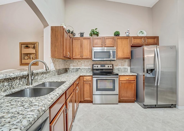 kitchen with arched walkways, light stone counters, stainless steel appliances, and a sink