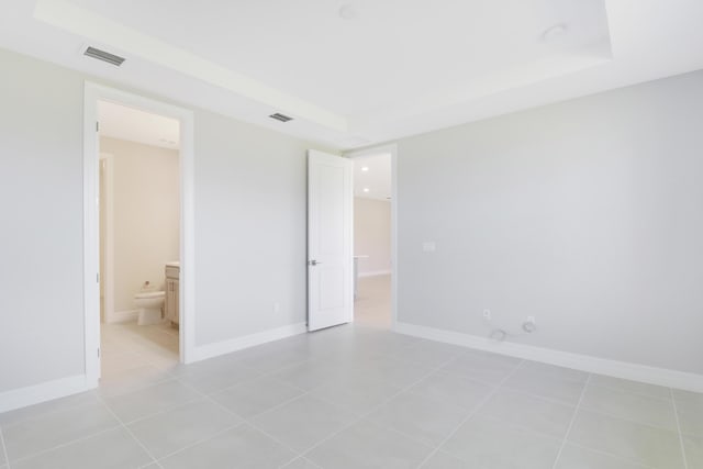 unfurnished bedroom with a tray ceiling, light tile patterned flooring, visible vents, and baseboards