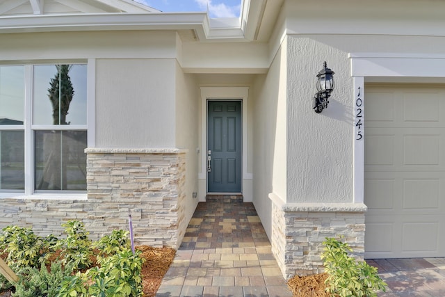 doorway to property with an attached garage, stone siding, and stucco siding