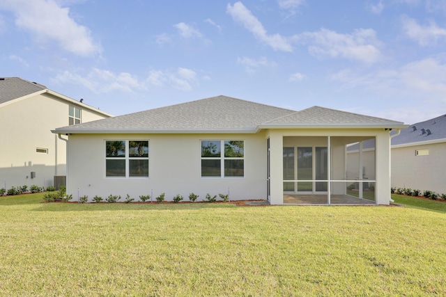 back of property with a shingled roof, a sunroom, a yard, and stucco siding