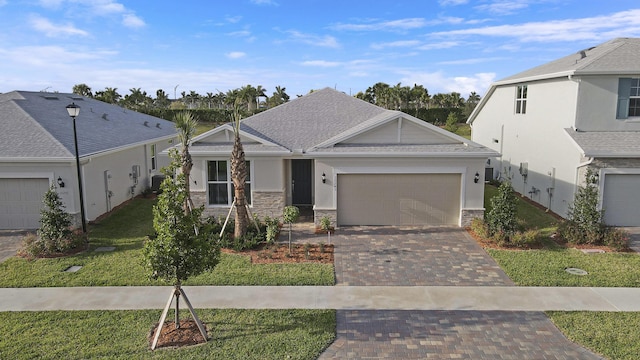 view of front of house featuring decorative driveway, a shingled roof, an attached garage, a front yard, and stone siding