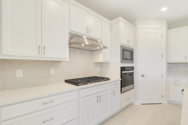 kitchen with under cabinet range hood, white cabinets, light countertops, appliances with stainless steel finishes, and decorative backsplash