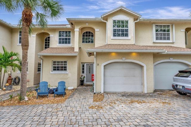 townhome / multi-family property with stucco siding, an attached garage, decorative driveway, and roof with shingles