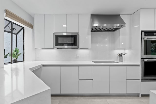 kitchen featuring wall chimney exhaust hood, modern cabinets, appliances with stainless steel finishes, light countertops, and white cabinetry