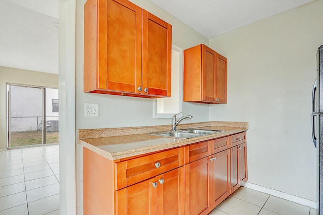 kitchen featuring brown cabinets, light countertops, light tile patterned flooring, a sink, and baseboards