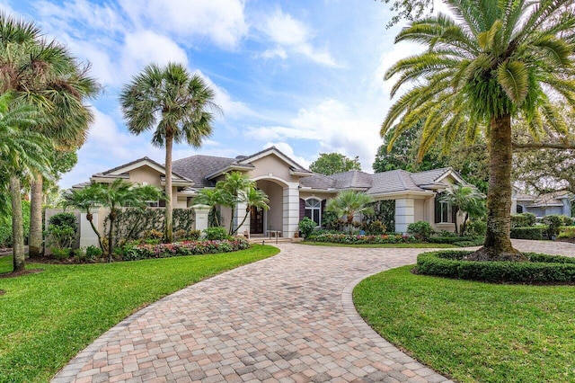 view of front of property with decorative driveway, a front yard, and stucco siding