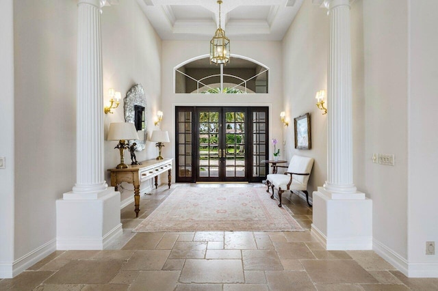 foyer featuring stone tile flooring, decorative columns, a towering ceiling, and baseboards