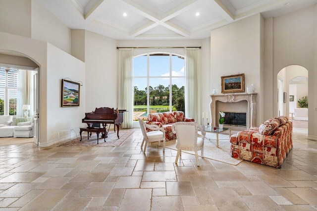 living room with arched walkways, stone tile floors, coffered ceiling, a towering ceiling, and beamed ceiling