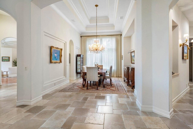 dining space featuring arched walkways, stone tile floors, a tray ceiling, an inviting chandelier, and crown molding