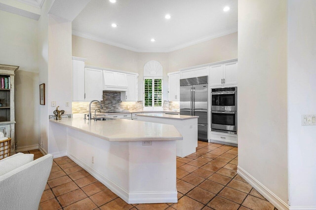 kitchen featuring stainless steel appliances, a peninsula, white cabinetry, light countertops, and backsplash