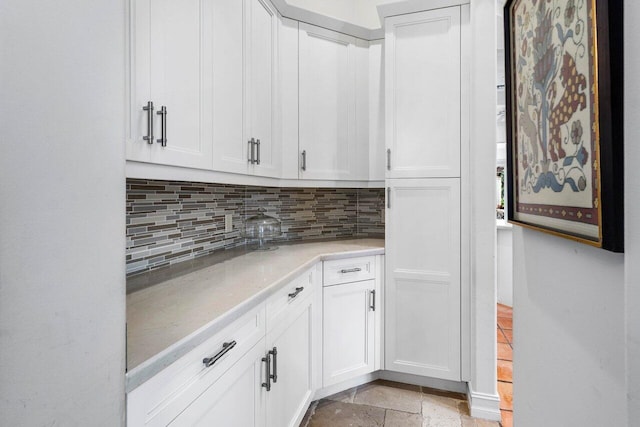 interior space with tasteful backsplash, white cabinets, light countertops, and stone finish flooring