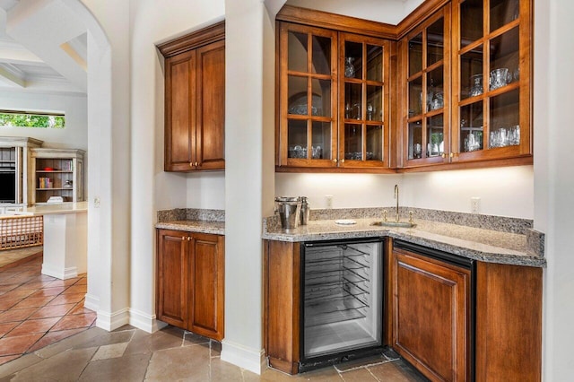 bar with wine cooler, stone tile floors, a sink, wet bar, and baseboards