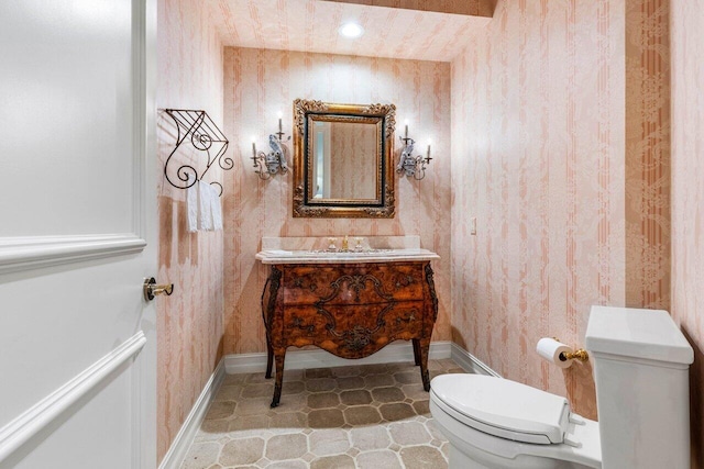 half bath with baseboards, vanity, toilet, and wallpapered walls