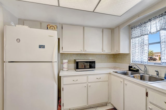 kitchen with stainless steel microwave, freestanding refrigerator, a sink, light countertops, and backsplash