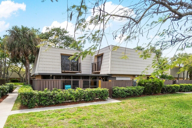 rear view of house featuring a lawn, a balcony, and fence