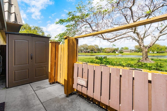view of gate with fence, an outbuilding, a storage shed, and a water view