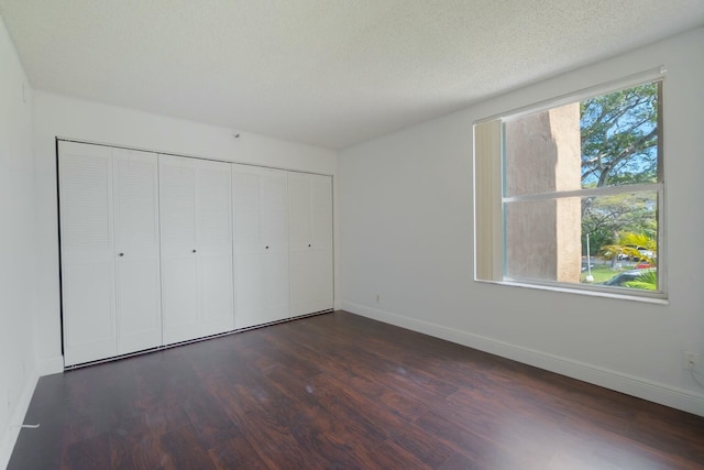 unfurnished bedroom featuring dark wood-type flooring, a closet, a textured ceiling, and baseboards