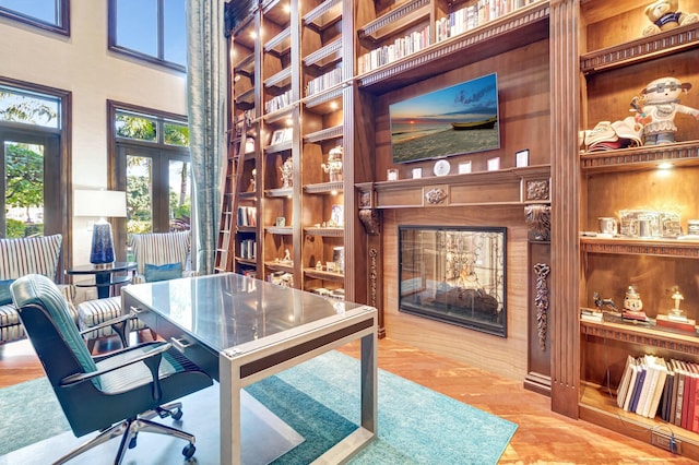 home office with built in shelves, wood finished floors, a towering ceiling, and a fireplace