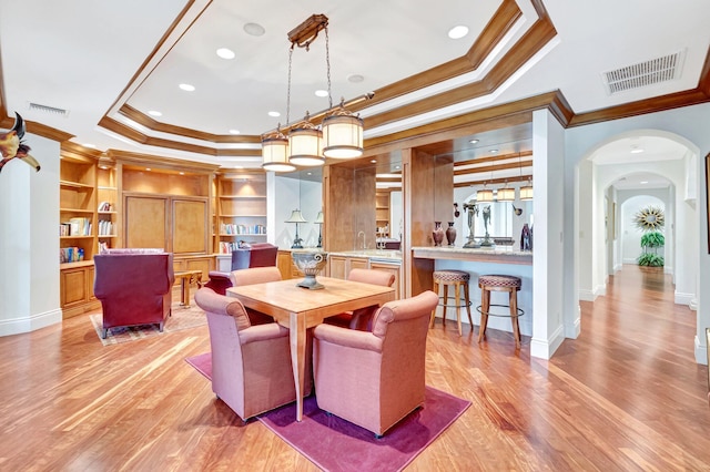 dining room featuring arched walkways, visible vents, light wood-style flooring, and a raised ceiling