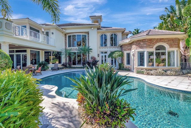 rear view of house with an outdoor pool, a patio area, stone siding, and stucco siding